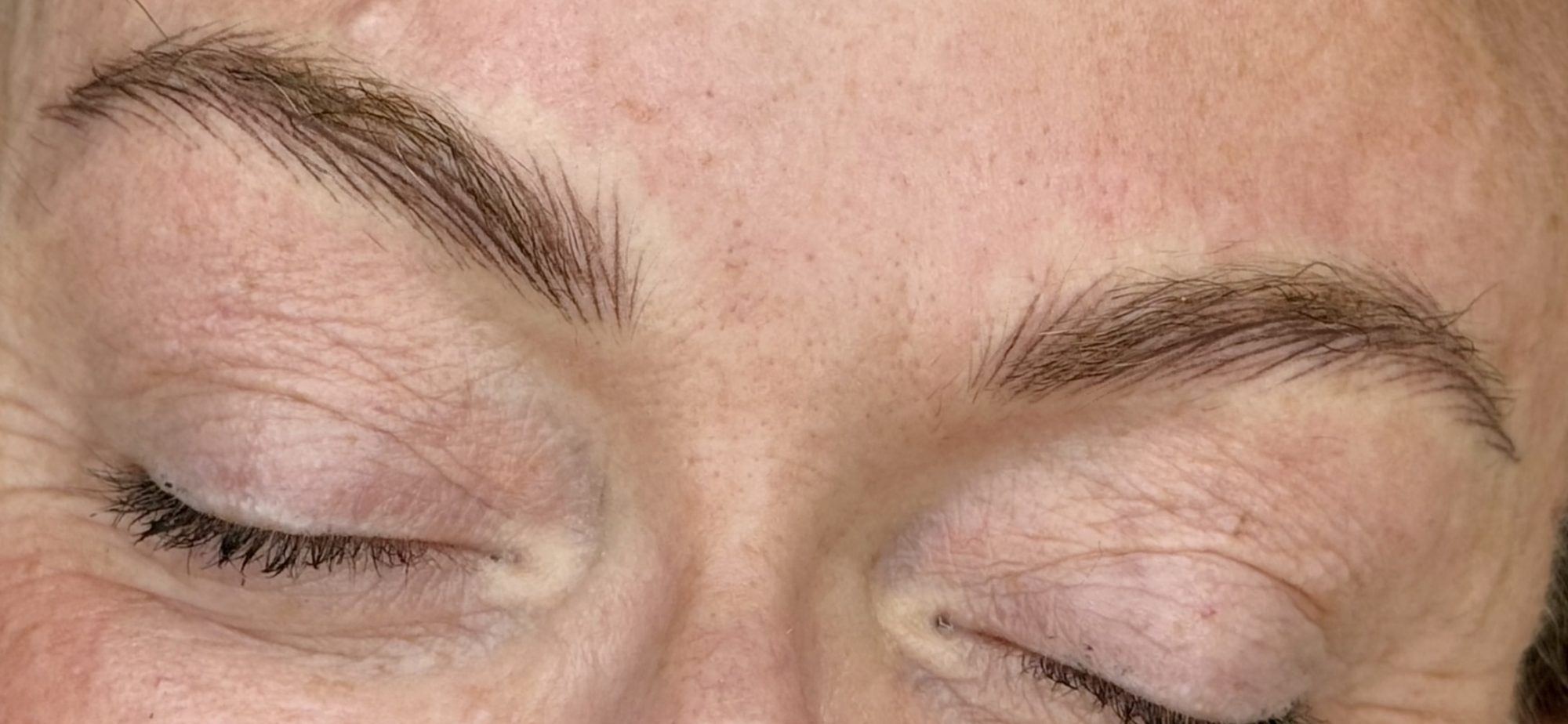 Both brows of a client with closed eyes, showing natural hair strokes